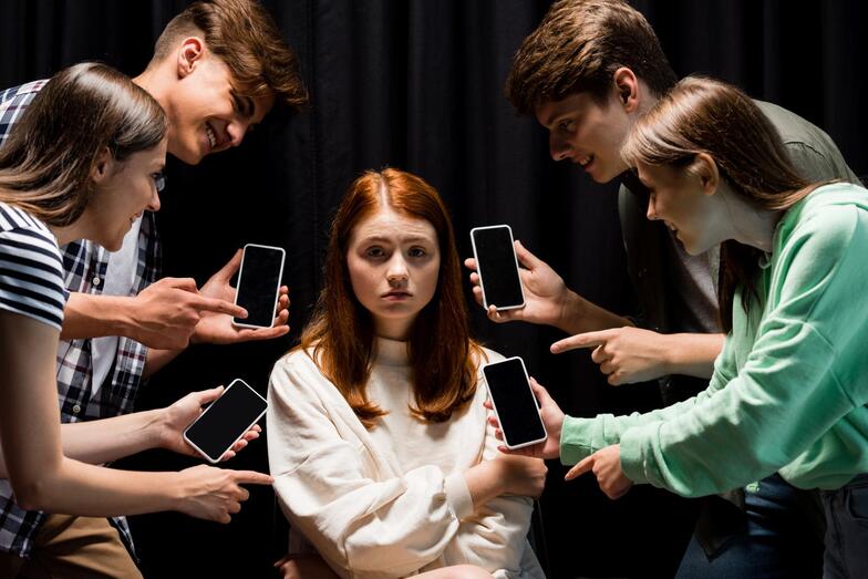 smiling teenagers pointing with fingers at girl during bullying and holding smartphones with blank